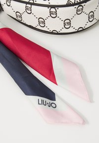 Hvid håndtaske med sort geometrisk mønster, parret med et silkebånd med røde, navy og lyserøde diagonale striber samt "LIU JO" logo.