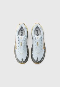 Μπλε και γκρι αθλητικά παπούτσια με κίτρινες λεπτομέρειες και υφή στην επιφάνεια, με επενδεδυμένο περιλαίμιο και κορδόνια για ασφαλή εφαρμογή. Εμπορικό σήμα HOKA.