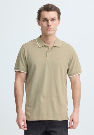 Beiges Poloshirt aus gewobenem Stoff, mit Kragen und kontrastierendem weißen Besatz sowie kurzen Ärmeln. Dezentes Logo auf der Brust.