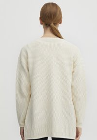 Kremowy sweter z teksturowanym wzorem, z długimi rękawami i luźnym krojem. Tył ma zaokrąglony dekolt i rozporki po bokach.