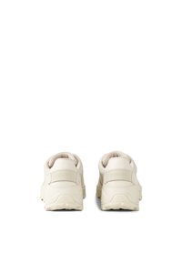 Beige athletic shoes with mesh and rubber materials, featuring a padded collar, textured sole, and logo detail on the heel.