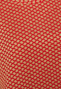 Rode en beige textiele stof met een herhalend geometrisch visgraatpatroon. Het ontwerp is geweven, wat een driedimensionaal effect creëert.