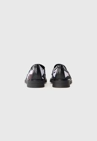 Pair of black and white cow-print loafers with black heels, shown from the back on a plain white background.