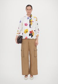 White shirt with colorful floral print, long sleeves; tan cargo pants with side pockets; brown clutch; cream pointed-toe shoes.