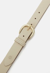 Curea din piele bej cu cataramă rotundă aurie și multiple găuri de ajustare pe fundal alb.