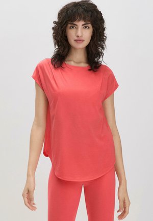 Korallefarbener Kurzarm-Top aus weichem Material mit lockerer Passform, rundem Ausschnitt und leicht verlängertem Rückensaum. Kombiniert mit passenden Leggings.