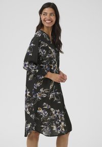 Rochie florală neagră cu modele în nuanțe de mov, albastru și bej. Dispune de un decupaj în V, mâneci lungi și o croială lejeră. Textură de material neted.