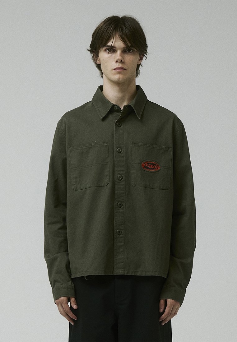 Olive green button-up shirt in a soft fabric, featuring two chest pockets and a red embroidered logo on the left side.