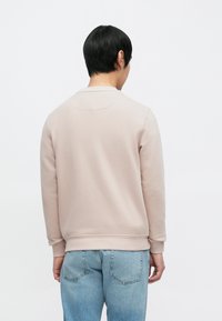 Lys rosa genser med lange ermer, rund hals og ribbestrikkede mansjetter, kombinert med lyseblå denimjeans. Myk tekstur og avslappet passform.