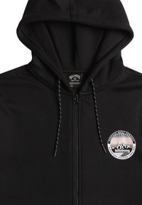 Felpa nera con zip realizzata in tessuto morbido, con cappuccio regolabile tramite cordino, toppa con logo sul lato sinistro del petto e cuciture a contrasto.