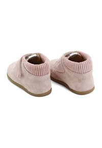Par de zapatos de bebé de ante rosa con puños acanalados en los tobillos y suelas de goma marrón, mostrados desde la parte trasera sobre un fondo blanco.