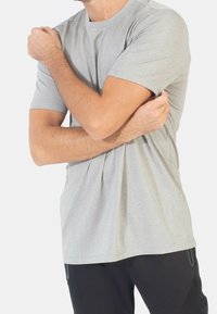 Světle šedé tričko s krátkým rukávem a texturovaným, žebrovaným vzorem. Kulatý výstřih a volný střih, kombinované s černými sportovními kalhotami.