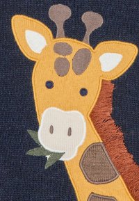 Gelber und brauner gestickter Giraffenkopf auf navyfarbigem Stoff, mit grünen Blättern im Mund und strukturierten Akzenten am Hals und den Flecken.