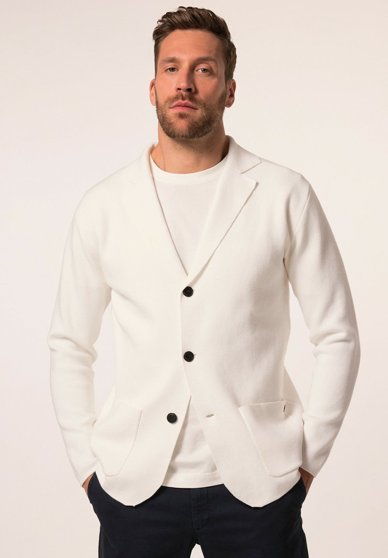 Blazer blanco de punto con botones negros, dos bolsillos frontales, cuello de muesca y diseño estilizado, usado sobre una camiseta blanca.