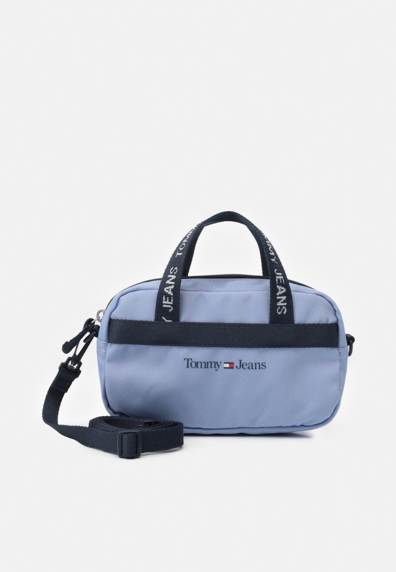 Sac en tissu bleu avec doubles poignées, une bandoulière amovible et une bande d'accent noire. Présente le logo "Tommy Jeans" sur le devant.