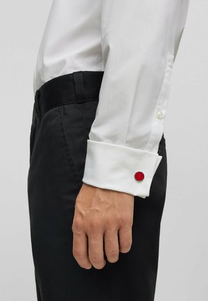 Valkoinen pitkähihaisena paita napillista hihansuutta ja punaisella pyöreällä korostuksella, yhdistettynä mustiin housuihin. Suuri kankaalle, slim fit -muotoilu.