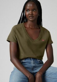 Camiseta verde oliva con escote en V y mangas cortas, hecha de tela suave, que presenta un pequeño logo rojo de Levi's en el lado izquierdo del pecho. Combinada con jeans azules.