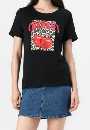 Kobieta ubrana w czarną koszulkę z czerwonymi wiśniami na tle w panterkę, zestawioną z niebieską spódnicą jeansową.