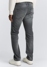 Jean en denim gris à coupe ajustée avec une texture légèrement décolorée. Équipé de deux poches arrière et d'une taille mi-haute, associé à des baskets blanches.