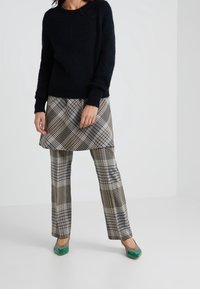 Maglione nero a maglia, gonna a quadri beige, nera e blu, con pantaloni a quadri abbinati; scarpe verdi con una texture lucida.