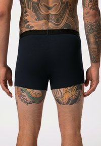 Boxer ajustados de color azul marino, hechos de una tela suave y con una cinturilla elástica negra. Los tatuajes corporales visibles realzan el aspecto general.