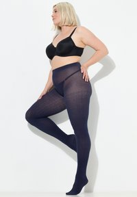 Granatowe, nieprzezroczyste rajstopy o prążkowanej fakturze i wysokim pasie zapewniającym wsparcie. Połączone z czarnym biustonoszem, podkreślającym sylwetkę nóg.