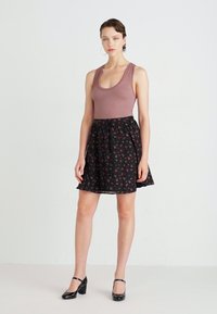 Top de tanque em mauve com nervuras, combinado com uma saia preta com pequenos padrões florais vermelhos. Modelo usa saltos pretos com tiras. Design simples e casual.