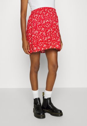 Saia floral vermelha com cintura elástica, até ao joelho, combinada com botas de cano curto pretas e meias brancas, numa modelo contra um fundo simples.