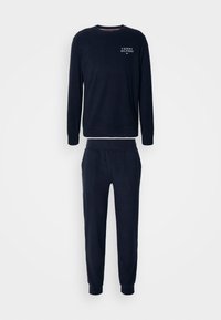 Námořnický modrý sportovní komplet vyrobený z měkkého materiálu, obsahující mikinu s kulatým výstřihem a kalhoty s elastickým pasem a žebrovanými manžetami. Logo na hrudi.