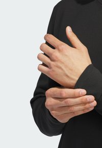 Black long-sleeve shirt with ribbed cuffs, close-up of hands adjusting the sleeve, showcasing smooth fabric texture and natural skin tones.