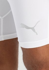 Hvit treningsshorts laget av elastisk stoff med en tettsittende design. Inkluderer en reflekterende grå Puma-logo på siden.