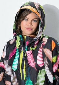 Barevná lehká bunda s černým podkladem a živými ptačími vzory v růžové, zelené, oranžové a bílé. Design s kapucí a zapínáním na zip.