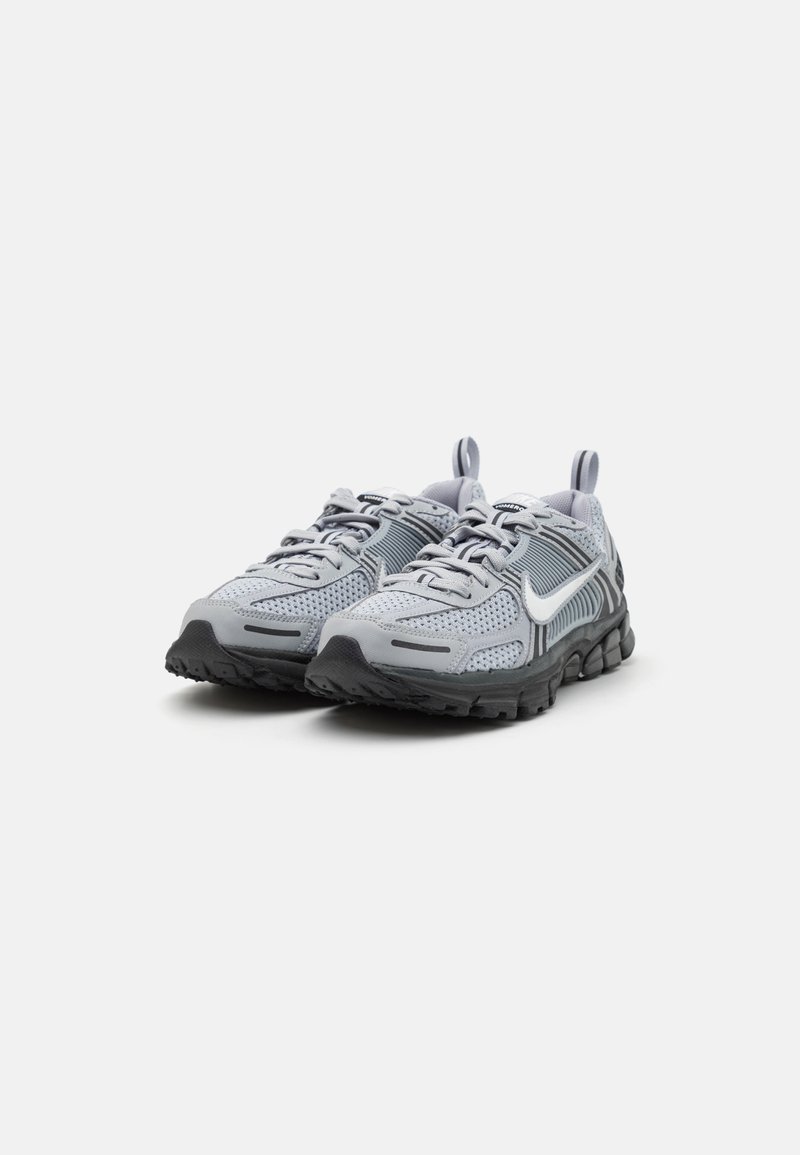 Graue Sportschuhe mit einem Obermaterial aus Mesh, geschichtetem Design und einer schwarzen Gummisohle mit sichtbaren Profilen. Inklusive Schnürsenkel und Ziehschlaufen.