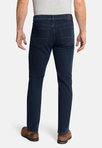 Dunkelblaue Denim-Jeans mit Slim-Fit, ausgestattet mit Gesäßtaschen und einem strukturierten Bund. Von hinten getragen mit braunen Stiefeln.