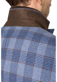 Kurtka w niebiesko-brązową kratę z kontrastowym brązowym kołnierzem, posiadająca różnorodne wzory i tekstury. Widoczne detale szycia.