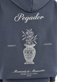 Sudadera con capucha oscura con ilustración de jarrón floral blanco y texto "Pegador", "Moments", "Memories" y "Moments to Memories" en la parte trasera.