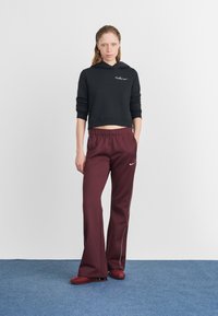 Melnā īsā kapuce ar Nike logo, kombinēta ar bordo platām biksēm ar baltām sānu strīpām un aukliņu viduklī.