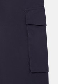 Material bleumarin închis cu un buzunar cargo dreptunghiular prevăzut cu clapetă și cusături vizibile pe partea dreaptă.