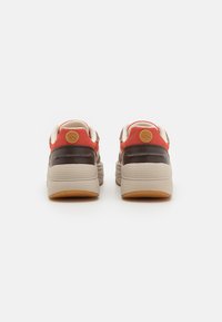 Sneakers z mieszanym materiałem, łączącym siateczkę w kolorze czerwonym i akcenty ze skóry w kolorze brązowym. Masywna beżowa podeszwa o teksturowanym wykończeniu.
