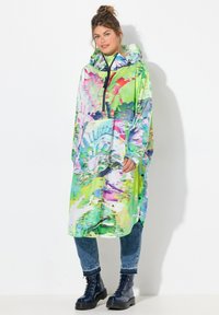Barevný pončo s kapucí a živými abstraktními vzory v zelené, růžové a modré barvě. Má půlzipový přední díl a volný střih. Vytvořeno ve spojení s tmavě modrými vojenskými botami.