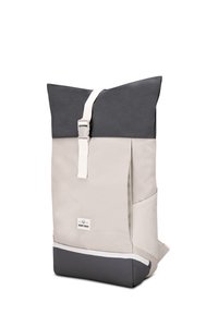 Sac à dos à rabat enroulable bicolore beige et gris foncé avec une sangle et une boucle blanches à l’avant, une poche latérale et un petit écusson logo.