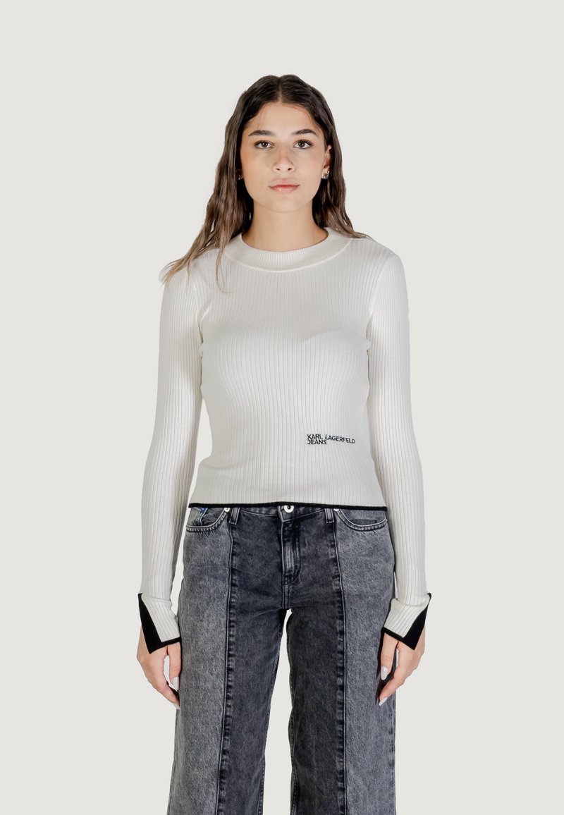Top blanco de manga larga con canalé, escote redondo y puños de acento negros. Presenta texto de logo impreso en la parte delantera. Combinado con jeans de pierna ancha grises.