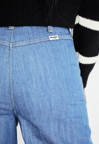 Lichtblauwe denim jeans met een lichte vervaging, voorzien van een witte Wrangler-label op de achterste tailleband en zichtbare stikdetails.