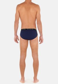 Marineblaue Herrenunterwäsche mit einem schwarzen elastischen Bund, der mit einem weißen Logo versehen ist. Glatter Stoff, figurbetonte Form und minimales Design für die Bedeckung.
