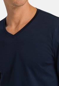 T-paita, tummansininen, V-pääntiellä, pehmeästä kankaasta, lyhyillä hihoilla ja sileällä pinnalla, jossa on minimaalinen ompeluympäristö.