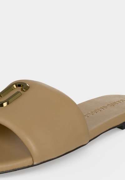 Μπεζ δερμάτινο σανδάλι slide με χρυσή μεταλλική λεπτομέρεια λογότυπου σε φαρδιά λουρά και επίπεδη μαύρη σόλα.