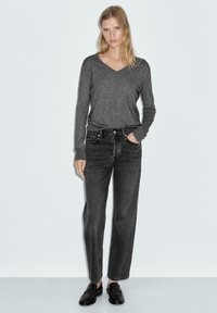 Maglietta grigia a maniche lunghe con scollatura a V, abbinata a jeans denim neri a vita alta. Mocassini neri completano l'outfit. Semplice, vestibilità rilassata.