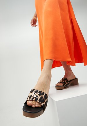 Sandali con plateau in stampa leopardo, con una fascia nera, tacco in legno e accento con logo argentato, abbinati a un vestito arancione.