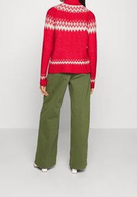 Red knit sweater with white diamond pattern, paired with green wide-leg pants. Sweater features a high neckline and ribbed cuffs.