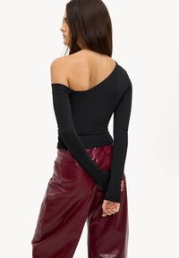 Zwarte top met lange mouwen en één schouder bloot, aansluitend ontwerp, en gestructureerde bordeauxkleurige faux leren broek met een glanzende afwerking.